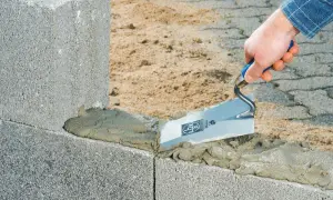 Maurer trägt Mörtel mit Kelle auf Betonsteine auf. Der Unterschied zwischen Beton und Zement wird hier beim Bau deutlich.