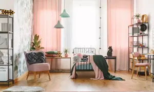 Ein stilvolles Jugendzimmer einrichten: Rosa Vorhänge, ein Bett mit Decken, ein Sessel mit Knoten-Kissen und ein Schreibtisch mit Regal.