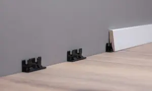 Schwarze Clips zur einfachen Montage von Sockelleisten an der Wand.