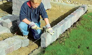 Mann setzt mit Hammer und Richtschnur präzise Rasenkantensteine, um den Garten zu gestalten.