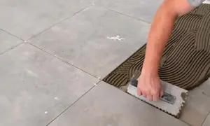 Hand spreadet Mörtel mit einer Kelle, um Fliesen zu verlegen. Kleine weiße Abstandshalter sorgen für gleichmäßige Fugen.