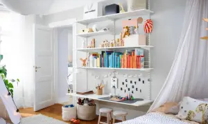 Ein schmal eingerichtetes Kinderzimmer mit einem Regal voller Bücher und Spielzeug, einem Schreibtisch und einem Bett mit Baldachin.