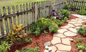 Natürliche Steinplatten formen einen geschwungenen Gartenweg, umgeben von bunten Blumen und grünen Pflanzen. Tolle Gartenweg Ideen für Ihr Zuhause.