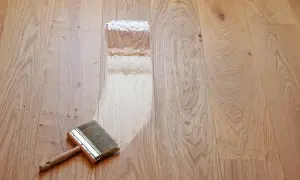Breite Pinsel trägt Lack auf einen hellen Holzdielenboden auf. Der Prozess, einen Dielenboden zu versiegeln, beginnt.