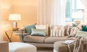 Ein beiges Sofa mit vielen Kissen, darunter gestreifte und florale Muster, lädt zum Entspannen ein.