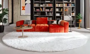Ein flauschiger, weißer Teppich liegt unter dem auffälligen, orangefarbenen Sofa und dem runden Couchtisch.