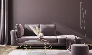 Ein gemütliches Wohnzimmer in mauve Farbe mit einem Samtsofa, einem geometrischen Couchtisch und einem Hocker.