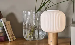 Eine skandinavische tischlampe holz mit geripptem Schirm und Holzfuß steht neben einem Glasvase mit Gräsern.