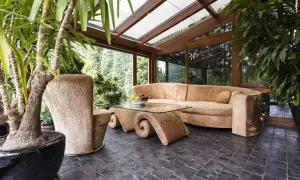 Gemütliches Ambiente im Wintergarten: Einladende Couch, geschwungener Glastisch und üppige Pflanzen laden zum Entspannen ein. Perfekt, um den Wintergarten einzurichten.