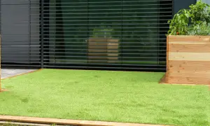 Frisch verlegter Kunstrasen bildet einen grünen Teppich vor einer modernen Hausfassade mit Jalousien und einem Holzpflanzkasten.