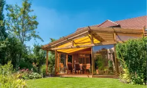 Ein moderner Wintergartenanbau mit Glasfront und gelbem Sonnensegel bietet tolle anbau wintergarten ideen. Gemütliche Sitzmöbel laden zum Verweilen ein.