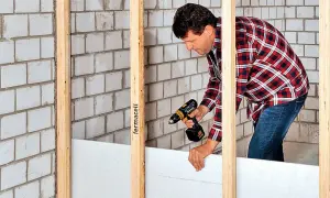 Mann baut eine Trennwand mit Gipskartonplatten und Akkuschrauber.