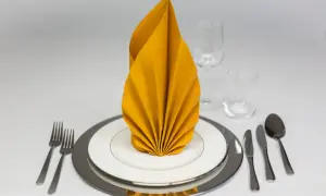 Elegante servietten falten: Ein gelber Fächer auf weißem Teller, umgeben von Besteck und Gläsern, bereit für ein festliches Mahl.