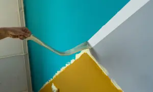 Hand zieht Klebeband ab, um eine gerade Kante zwischen türkisfarbener und grauer Wand zu schaffen. So gelingt das **richtig streichen**.
