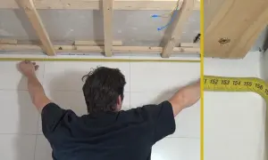 Mann misst die Decke für das Anbringen von Deckenpaneelen. Holzlatten sind bereits montiert.