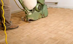 Mann schleift Parkett mit einer Maschine. Der Boden wird für eine neue Oberflächenbehandlung vorbereitet.