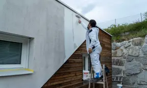 Mann streicht mit Rolle eine Hausfassade. So streicht man eine Fassade: Schritt für Schritt zum neuen Look.