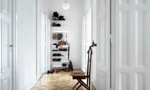 Helle Türen und ein weißes Regal lassen den schmalen Flur optisch breiter wirken. Schuhe und Hüte sind ordentlich verstaut.