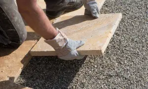 Arbeiter verlegt sorgfältig eine helle Terrassenplatte auf Kies.