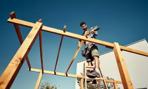 Mann auf Leiter schraubt Holzkonstruktion für ein Terrassendach selber bauen.