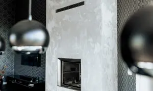 Edler Kamin mit Wischtechnik Wand in Grau. Daneben eine Wand mit geometrischem Muster und ein Teil einer Hängeleuchte.