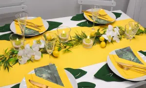 Sommerliche tischdeko mit zitronen, Orchideen und Kerzen. Gelbe Servietten und goldene Besteckteile runden das Bild ab.