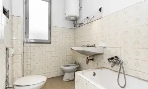 Badezimmer mit veralteten Fliesen, bereit zum Streichen. Toilette, Waschbecken und Badewanne sind sichtbar.