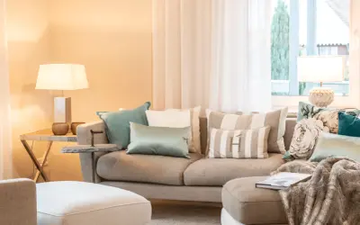 Ein beiges Sofa mit vielen Kissen, darunter gestreifte und florale Muster, lädt zum Entspannen ein.