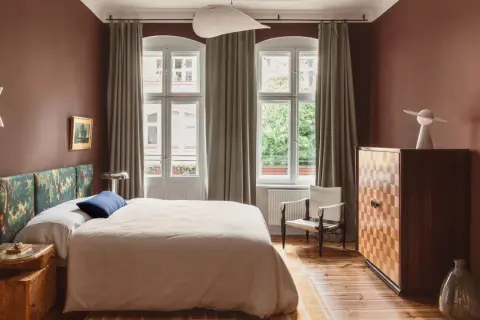 Ein Schlafzimmer in warmen, gedeckten Farben. Braune Wände, ein gemustertes Kopfteil und ein helles Bett schaffen eine gemütliche Atmosphäre.