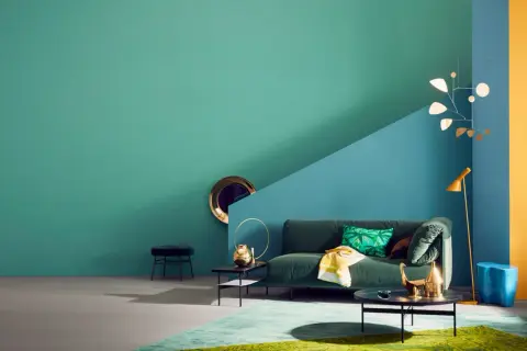 Ein Wohnzimmer mit petrolfarbener Wand, die zu einem blauen und gelben Bereich übergeht. Welche Farbe passt zu Petrol? Hier: Grün, Gold und Blau.