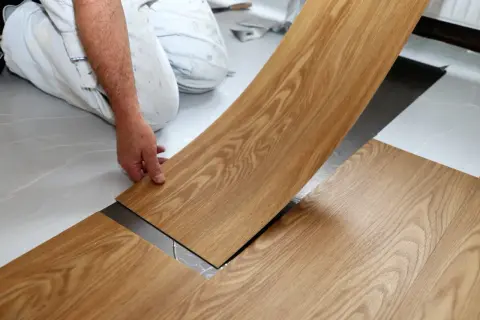 Hand verlegt Holzoptik-Vinylboden. Die Dielen werden präzise nebeneinander gelegt, um ein schönes Ergebnis zu erzielen.