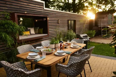 Eine schmale Terrasse gestalten: Gemütlicher Essbereich mit Holztisch, Rattanstühlen, Grill und Sitznische mit Kissen.