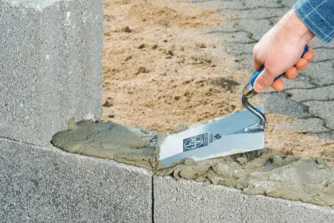 Maurer trägt Mörtel mit Kelle auf Betonsteine auf. Der Unterschied zwischen Beton und Zement wird hier beim Bau deutlich.