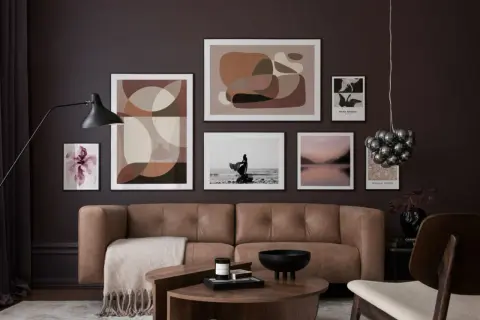 Ein braunes Ledersofa vor einer Wand mit abstrakter Kunst und einem Foto. Welche Farbe passt zu Schwarz? Hier: Braun und Beige.