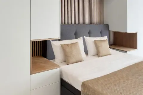Ein gemütliches kleines Schlafzimmer einrichten mit einem Bett, grauem Kopfteil, weißen und goldenen Kissen, Holzakzenten und weißen Schränken.