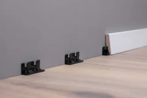 Schwarze Clips zur einfachen Montage von Sockelleisten an der Wand.