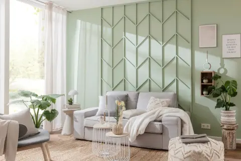 Moderne Wandgestaltung im Wohnzimmer hinter der Couch mit geometrischen Mustern in Mintgrün. Gemütliche Couch mit Kissen und Decke.