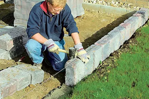 Mann setzt mit Hammer und Richtschnur präzise Rasenkantensteine, um den Garten zu gestalten.