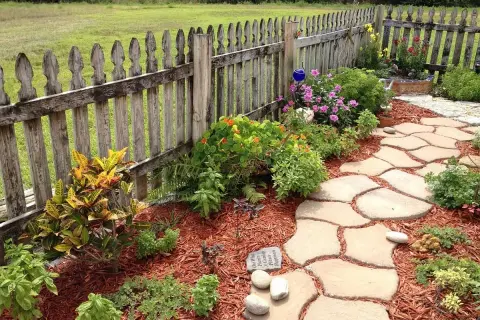 Natürliche Steinplatten formen einen geschwungenen Gartenweg, umgeben von bunten Blumen und grünen Pflanzen. Tolle Gartenweg Ideen für Ihr Zuhause.
