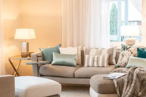 Ein beiges Sofa mit vielen Kissen, darunter gestreifte und florale Muster, lädt zum Entspannen ein.
