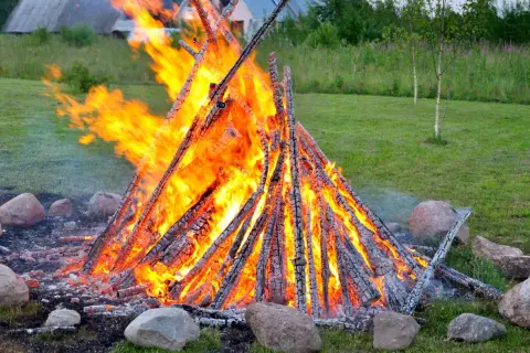 Ein großes, loderndes lagerfeuer im garten, umgeben von Steinen. Die Flammen tanzen hoch und erhellen die grüne Wiese.
