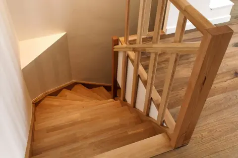 Holztreppe mit geschwungenen Treppenstufen. Der Handlauf und die Stufen sind aus hellem Holz gefertigt, was den Eindruck von Wärme und Natürlichkeit vermittelt. Die Treppenstufen streichen ist hier nicht nötig, da das Holz bereits schön zur Geltung kommt.