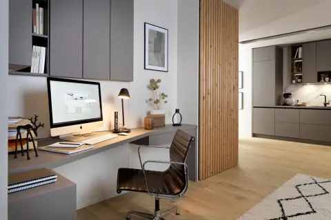 Moderne homeoffice ideen: Ein aufgeräumter Schreibtisch mit iMac, Lederstuhl und Regalwand. Daneben eine Holzwand, die in eine Küche übergeht.