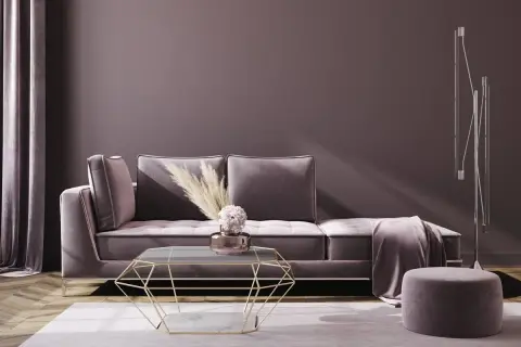 Ein gemütliches Wohnzimmer in mauve Farbe mit einem Samtsofa, einem geometrischen Couchtisch und einem Hocker.