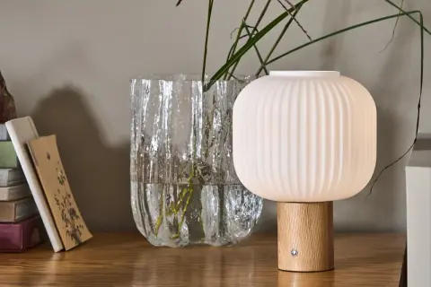 Eine skandinavische tischlampe holz mit geripptem Schirm und Holzfuß steht neben einem Glasvase mit Gräsern.