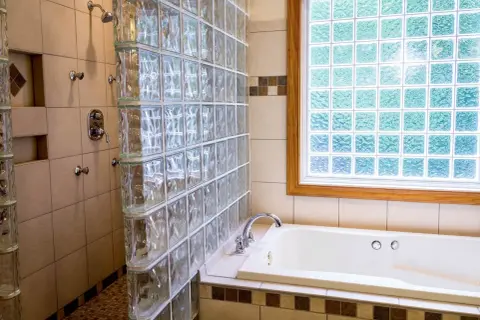 Badezimmer mit Dusche und Badewanne, umgeben von Glasbausteinen. Die Glasbausteine verlegen schafft ein helles und modernes Ambiente.