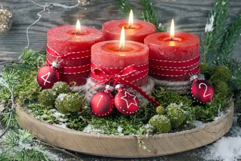 Ein **ausgefallener Adventskranz** mit vier roten Kerzen, geschmückt mit Moos, Tannenzweigen und kleinen Kugeln mit den Zahlen 1, 2, 4.
