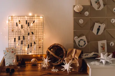 DIY Adventskalender Ideen: Ein Drahtgitter mit nummerierten Zetteln und Lichterkette, daneben braune Briefumschläge mit Weihnachtsmotiven.