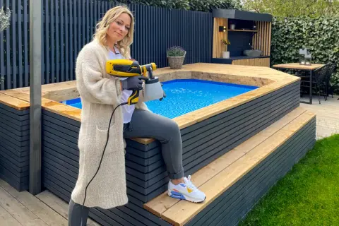 Frau mit Sprühgerät verkleidet aufstellpool mit Holz.