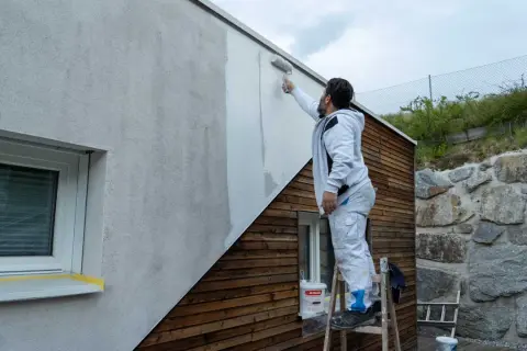 Mann streicht mit Rolle eine Hausfassade. So streicht man eine Fassade: Schritt für Schritt zum neuen Look.